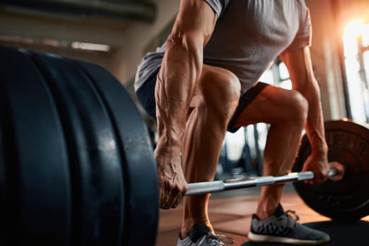 An elderly man is engaged in a strength training exercise, lifting a barbell with weights at a gym. This workout takes place during the afternoon, promoting fitness and health.