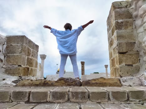 Tourist stands with arms wide open at ancient ruins, embracing the beauty of the location on her travel excursion.