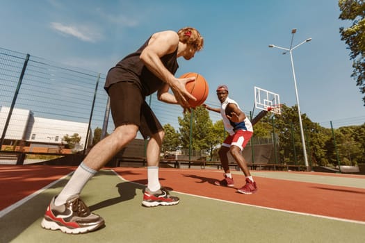Two young sportsmen playing basketball at outdoor court on sunny summer day