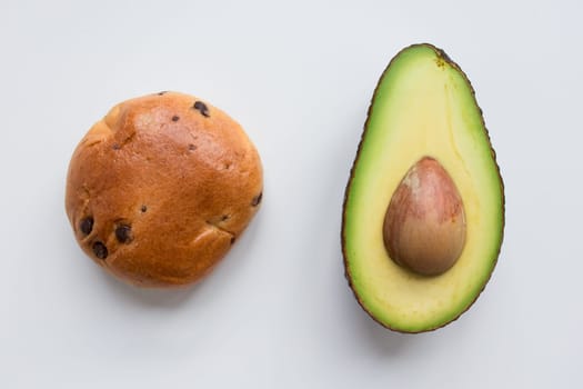 Chocolate chip bun and sliced avocado on white background.