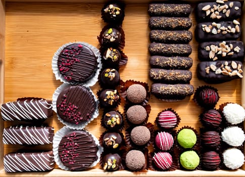 Assorted chocolate desserts on wooden tray with truffles and eclairs.