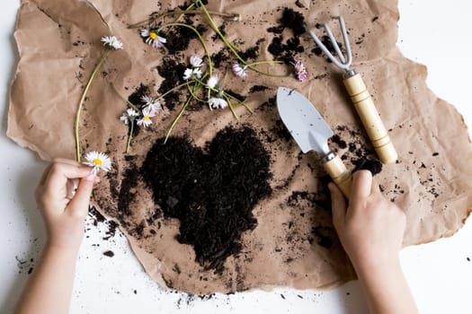 Gardening enthusiast tending floral heart arrangement on brown paper with tools.