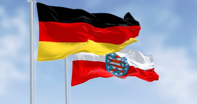 German national flag and Thuringia state flag fluttering side by side under clear sky. A symbol of federal unity, heritage, and identity. 3d illustration render. Rippled fabric.