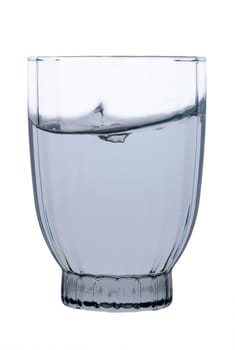 Droplets scatter as a splash disrupts the calm surface of translucent water in a uniquely shaped glass. Soft light accentuates the glass's contours, creating a moment of tranquil beauty.