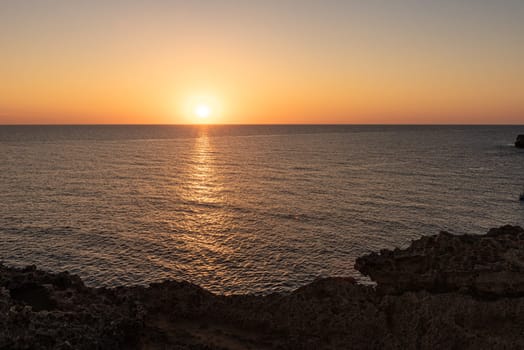 The serene sea at dawn or dusk, with calm, tranquil waters.Orange sky, clear skies, calm waters, rocks, empty space, Mediterranean Sea.