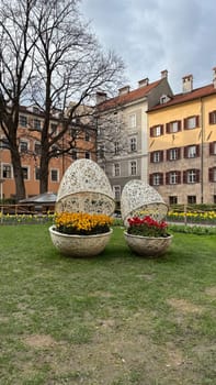 Beautiful Urban Outdoor Display With Decorative Floral Arrangements in Wicker Shapes in Innsbruck. Urban park scene featuring contemporary floral arrangements within decorative wicker structures, surrounded by colorful blooms and traditional architecture backdrop.