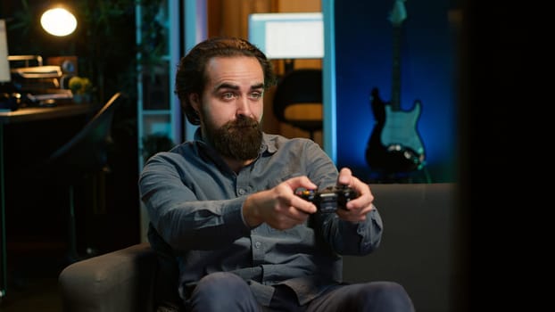 Man enjoying playing videogame in neon lit room, holding controller. Gamer participating in internet esports competition using professional gamepad for better victory chances, camera A