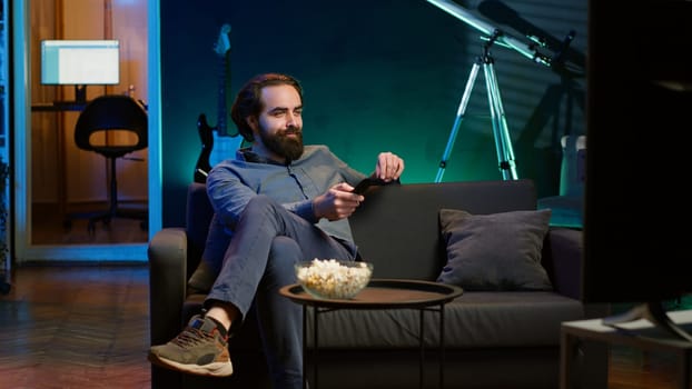 Man entering room, eating popcorn while watching interesting movie on streaming service, enjoying time off. Person coming home to looking at films broadcasted on TV and consume snacks, camera A