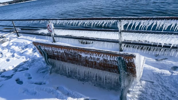 A beautiful wooden bench, adorned with glistening icicles, sits elegantly by the sea. Surrounded by soft, white snow and sparkling ice, it creates a peaceful winter scene, inviting quiet reflection.