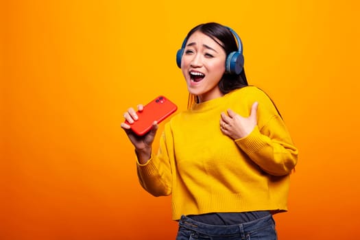 Excited woman with headphones, sings along to her favorite song, holding her cellphone like a microphone. Female individual using mobile device for a solo performance with joy and enthusiasm.