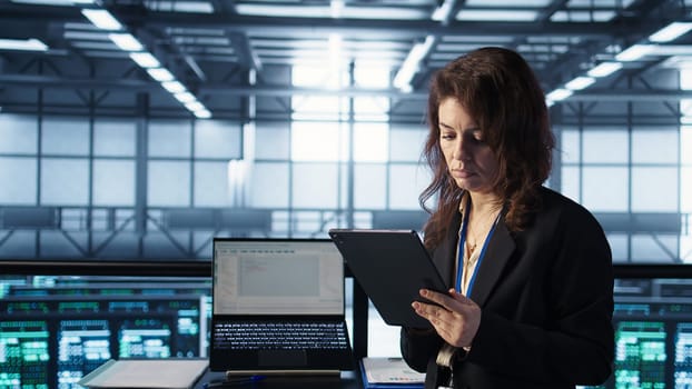 Admin in data center using artificial intelligence tech on tablet to deploy new server architectures. Woman in server room updating storage arrays to maintain stable performance, camera B