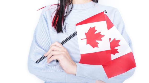 Unrecognized girl student in blue shirt holding small Canadian flag over gray background, Canada day, holiday, vote, immigration, tax, copy space.