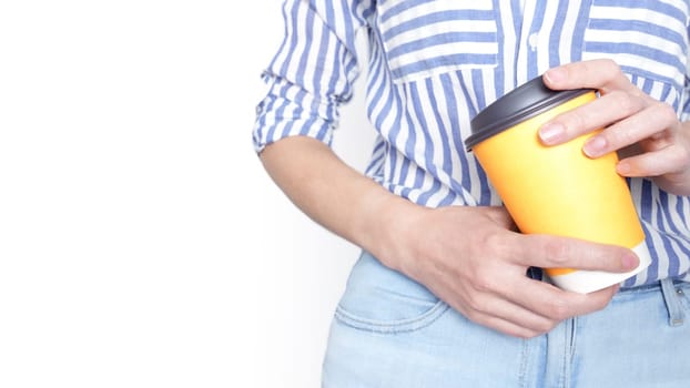 Woman holding a yellow mockup coffee cup with a black lid in front of her lower abdomen.