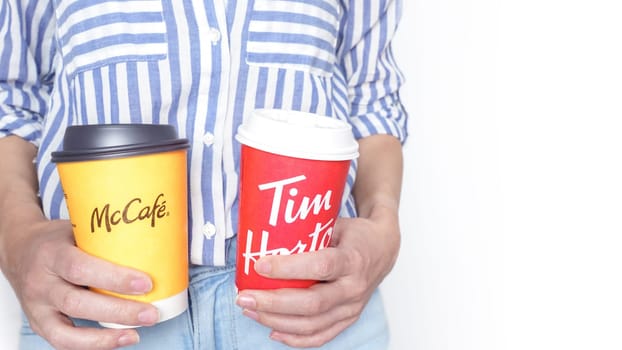Close-Up Image of a Woman Holding Two Paper Coffee Cups of McDonalds and Tim Hortans in Her Hands with Lids: Ottawa ON Canada - 2024-10-28