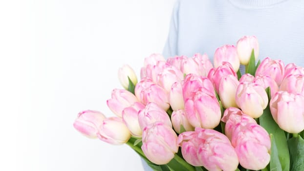 Woman holding a beautiful bouquet of vibrant pink tulips with green foliage against a white background. The pink tulips are striking and complement the womans attire perfectly.