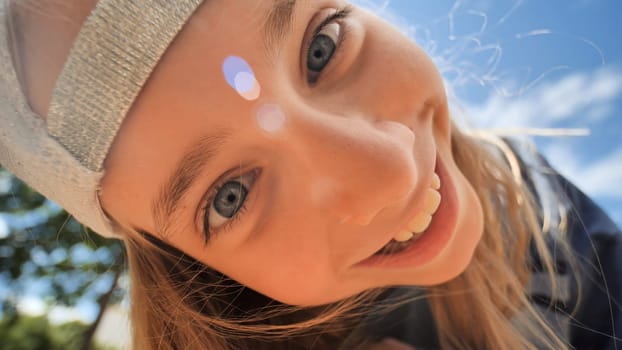 Portrait of a cheerful school girl wearing a white baseball cap, smiling broadly and showing her blue eyes on a bright sunny day