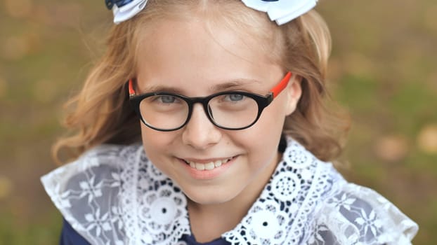 Close up portrait of a cheerful schoolgirl with glasses and a white lace collar, smiling outdoors, exuding happiness and confidence