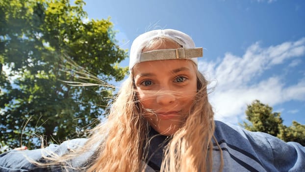 Portrait of a cheerful school girl wearing a cap, enjoying a sunny and windy day in a park, with her hair flowing freely