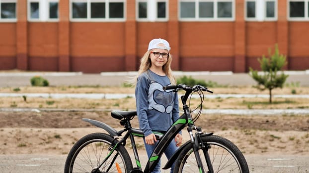 School girl standing with her bicycle in front of a school building, enjoying a sunny day