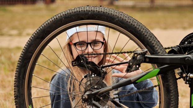 An eleven-year-old girl twists and looks at the wheel of her bicycle