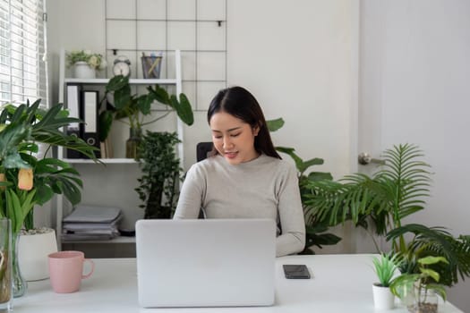 A woman sits intently at her desk, using her laptop to complete tasks, highlighting the productivity of a serene work environment filled with plants.