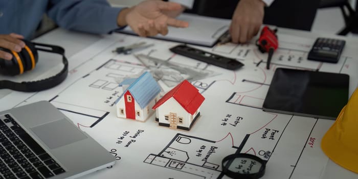 A group of architects examine miniature house models and detailed blueprints while brainstorming designs in a vibrant workspace.