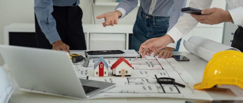 A team of professionals collaborates on construction blueprints, employing tools and models to visualize their project. They engage actively in discussions to enhance planning accuracy.