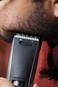 A person is using a hair clipper to trim facial hair carefully.