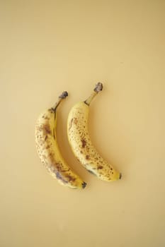 Two ripe bananas with brown spots arranged on a plain light backdrop.