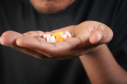 A person displays colorful pills in their open palm against a dark background.