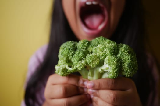 A child joyfully shows off a bunch of broccoli with a big smile.