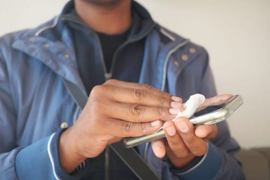 Person cleans their smartphone screen with a disinfecting wipe indoors.