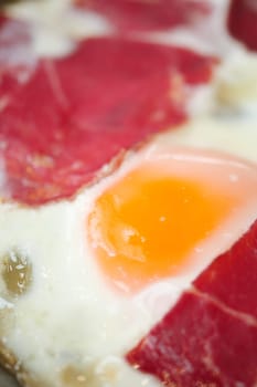 Close view of a vibrant egg yolk surrounded by cured meat for breakfast.