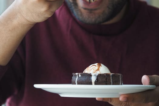 A man savors a slice of chocolate cake topped with ice cream.