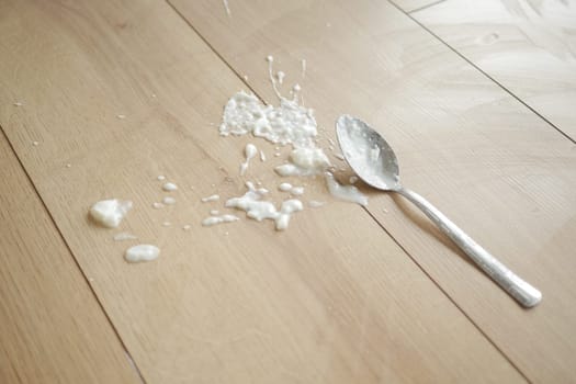 Spilled yogurt on wooden floor with spoon ,