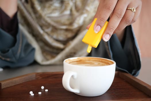 A person is pouring sweetener into a cup of coffee at a cafe table.