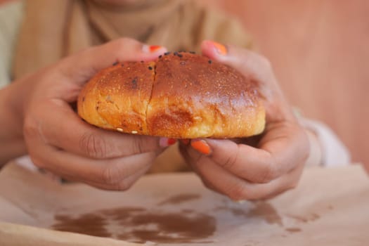 A person holds a warm, fresh bread roll with toppings in their hands.