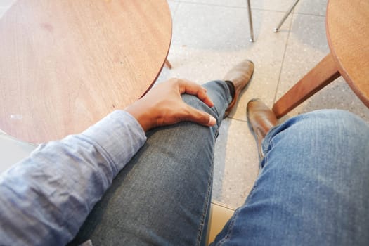 Person in jeans relaxes with hand on knee at a cozy cafe table.