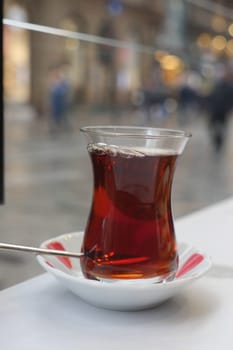 Hot Turkish tea in a delicate glass cup sits on a plate in a bustling area.