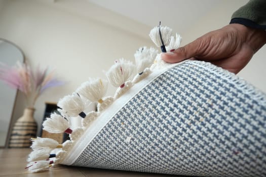 A person carefully unrolling a decorative rug in a bright room.