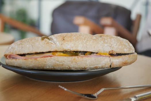 A freshly made sandwich with layers of ham, cheese, and pickles on a plate.
