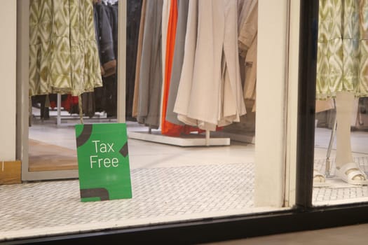 Shoppers explore a clothing store featuring tax free signs and summer styles.