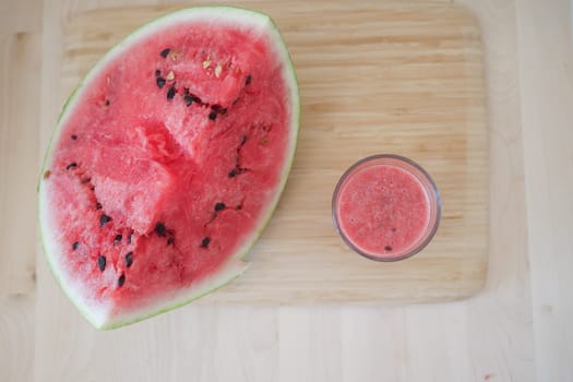 Sliced watermelon and a glass of freshly made juice sit on a cutting board.