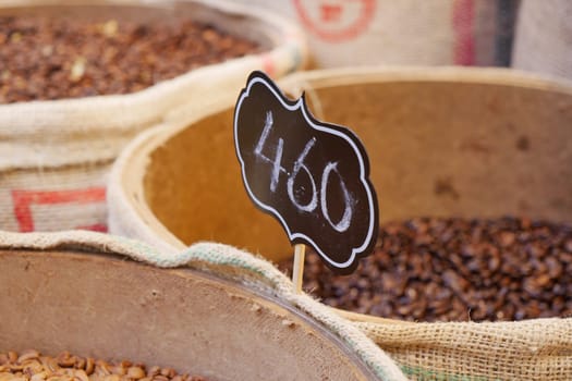 Various types of spices in containers at a market with a price sign.