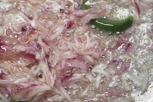 Chopped onions and green peppers fry in hot oil, creating bubbles.