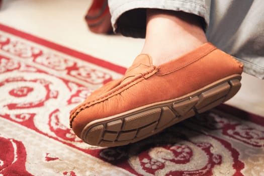 A person relaxes at home with a leather slipper on a decorative rug.
