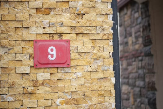 A bright red nine is on a textured yellow wall by a stone structure.