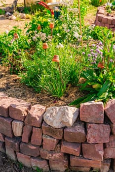 Herb spiral made of bricks for a small garden. Non-English translation: garlic, sorrel