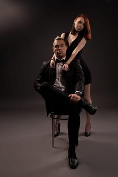couple portrait of woman in dress dominant man with handcuffs sitting on chair while enjoying foreplay during BDSM session