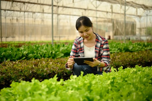 Female farmer in plaid shirt using digital tablet to analyze crop conditions in greenhouse.